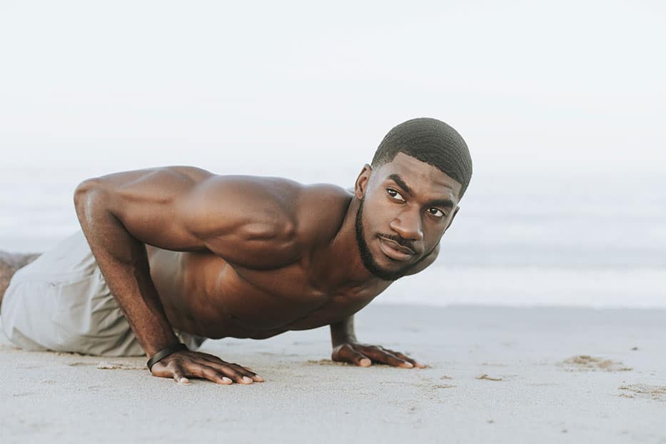 A man doing press ups on the beach.