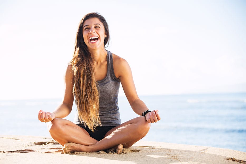 A laughing, young woman on the beach in a yoga pose.