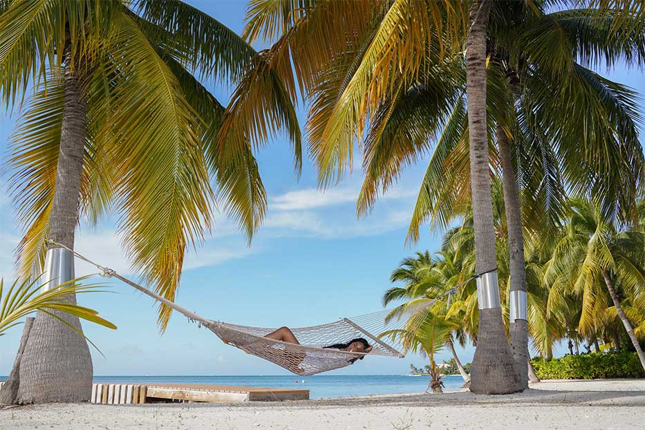Woman in a hammock between two palm trees with the Caribbean Sea in the background.
