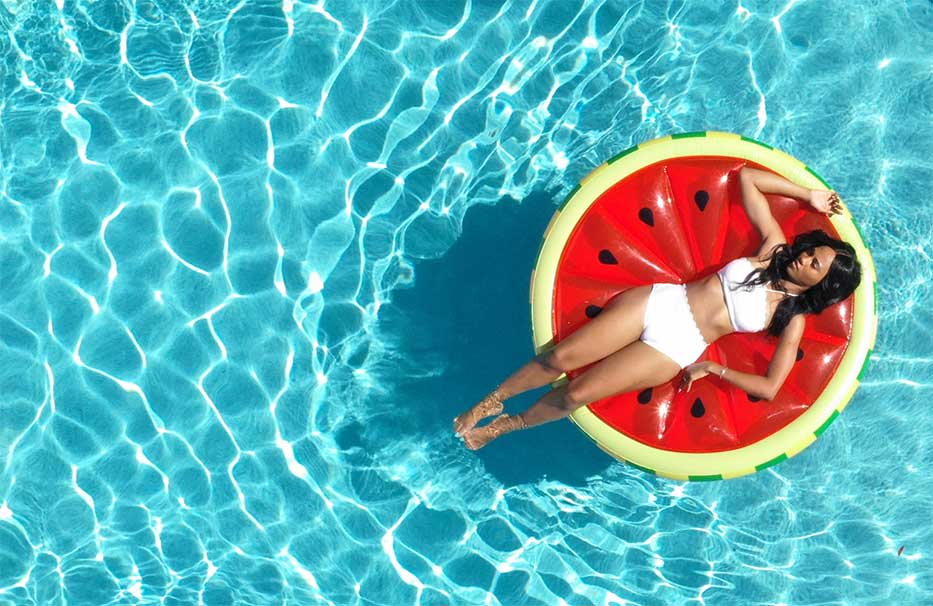 Caymanian girl floating in a pool on a watermelon slice lilo.