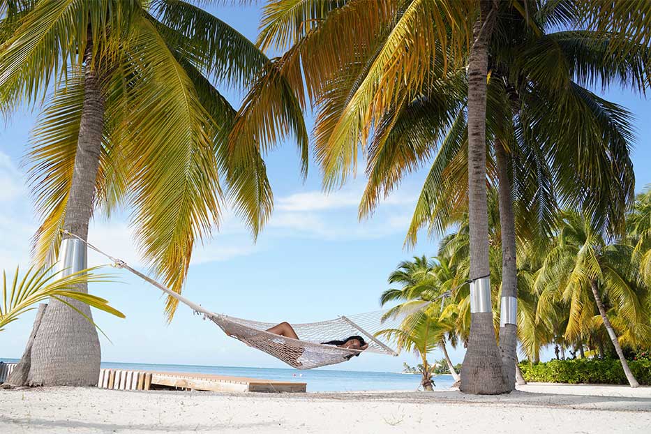 Lady relaxing in a hammock under plams trees in the Cayman islands.