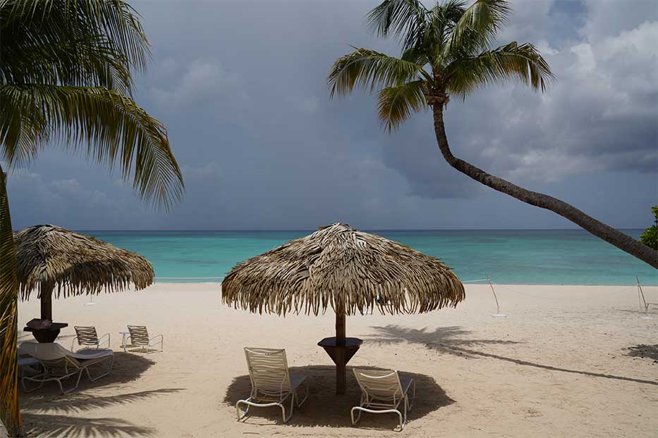 Thatched beach umbrellas and chairs Seven Mile Beach looking out towards the Caribbean Sea