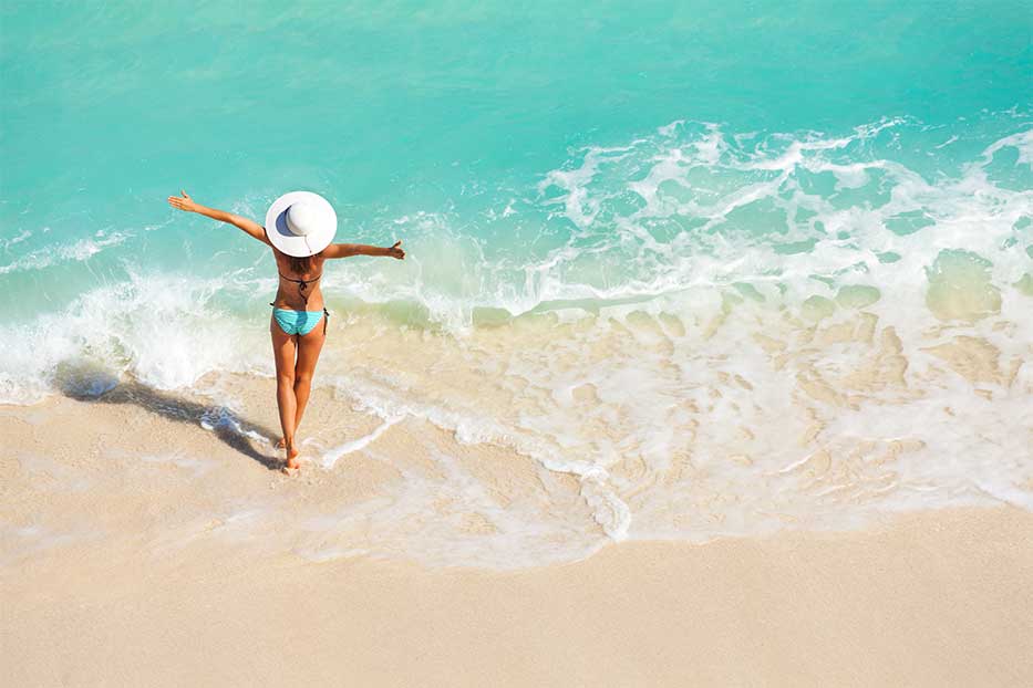 Woman standing arms out stretched on Seven Mile Beach in the Cayman Islands