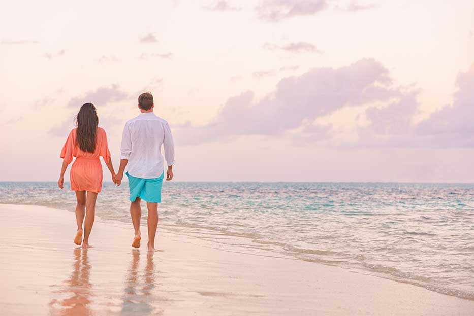 A couple walk hand in hand along the beach at sunset