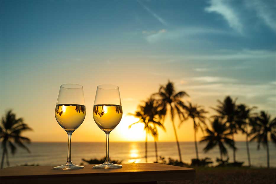 Glasses of white wine at sunset with palm trees in background